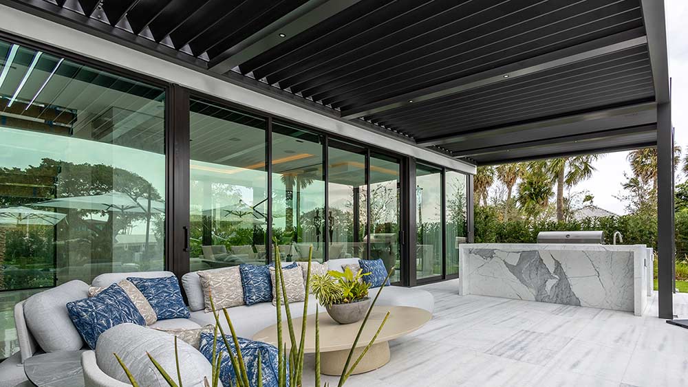 Large pergola in a residential setting: Modern black powder coating, attached to the house with automated louvered roof (Model R-BLADE by Azenco).