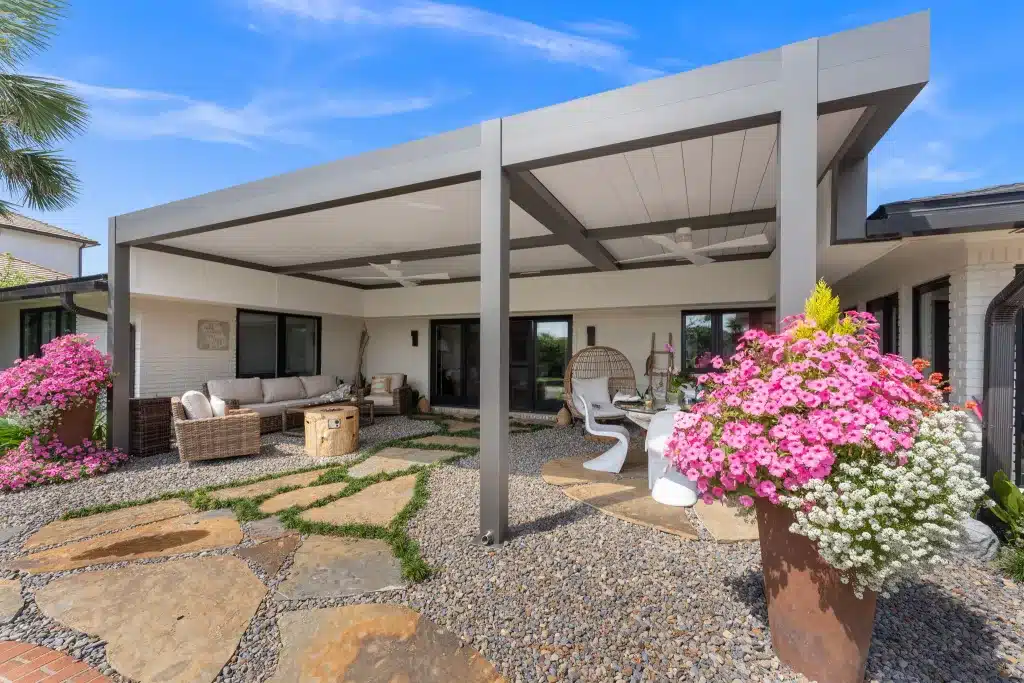 Luxury patio featuring a dark gray Azenco R-BLADE™ louvered pergola with cantilever posts, integrated fan, and LED lighting.