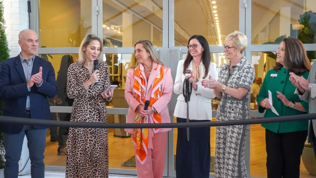 A ribbon-cutting ceremony moment at the Broad Hall event opening during High Point Market. Five women and one man stand in a line, with one woman speaking into a microphone, celebrating the debut of the innovative space.