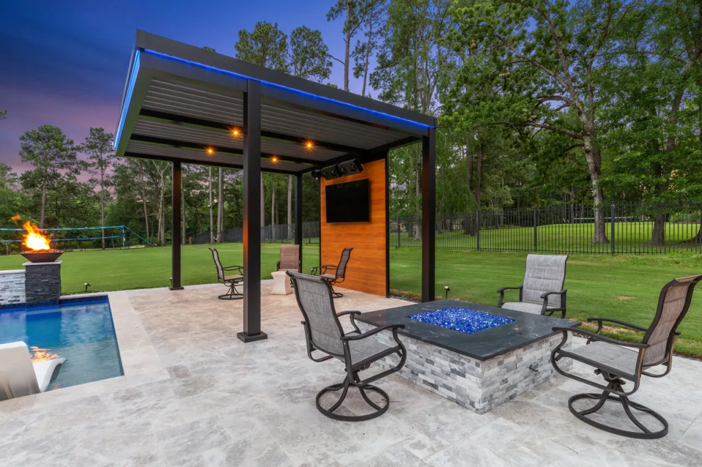 Angled view of the black R-Blade pergola cabana, showcasing the wood-grain accent wall, TV, and pool area with lounge chairs.