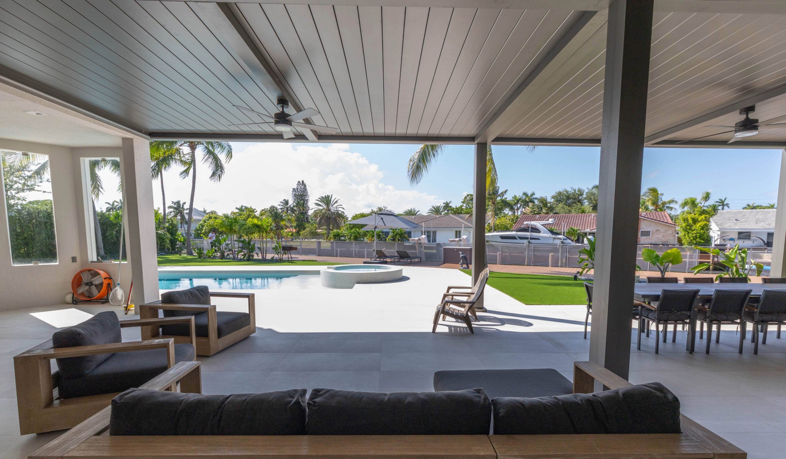 Covered patio with lounge seating, ceiling fans, and a dining area overlooking a pool and waterfront.